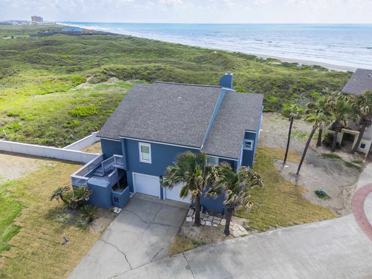 Beachfront vacation home with ocean views, nestled among coastal dunes and tropical palms just steps from pristine sandy shores.