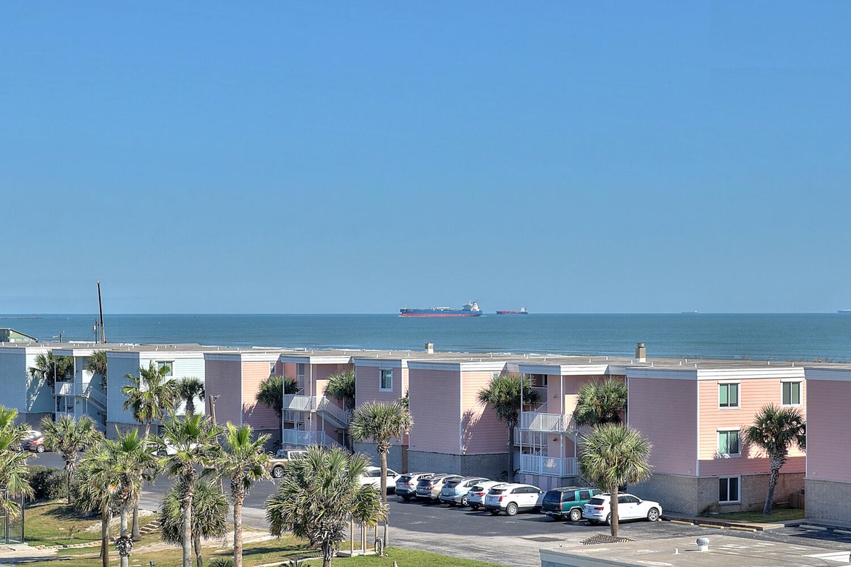 Coastal property buildings with palm trees and ocean views in the background. Parking available on-site.