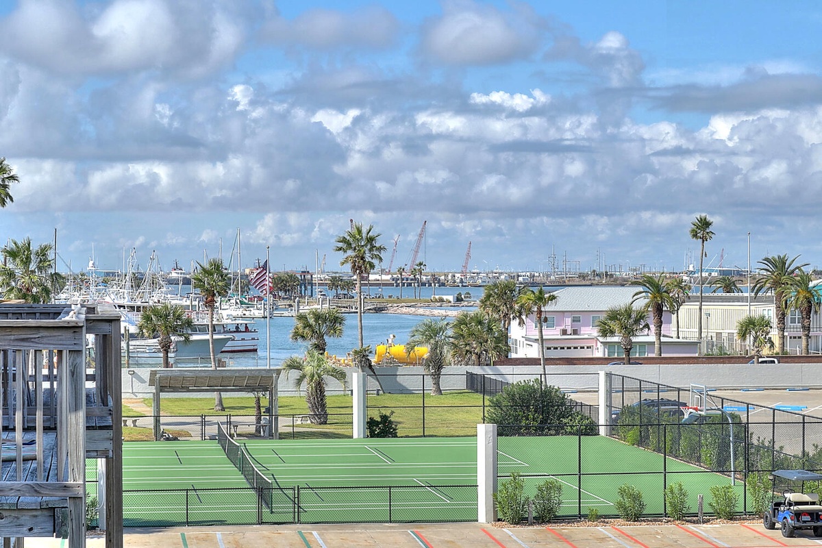 Balcony view of the waterfront tennis courts, marina, and palm trees.