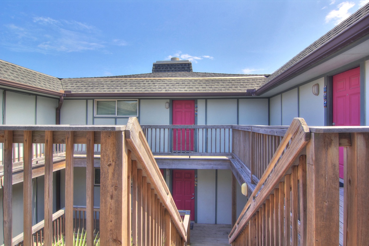 Multi-level property building with distinctive pink doors and wooden railings under blue skies.