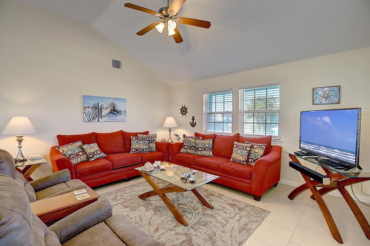 Relax in your spacious living room with plush red sofas, coastal décor, and modern entertainment setup.