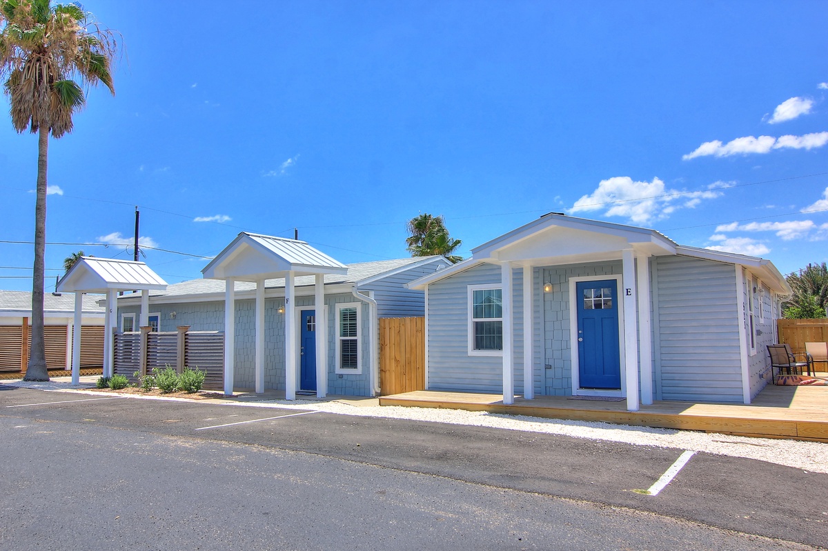 Modern coastal-style cottages featuring bright blue doors and contemporary design, set beneath clear Florida skies with palm trees nearby.