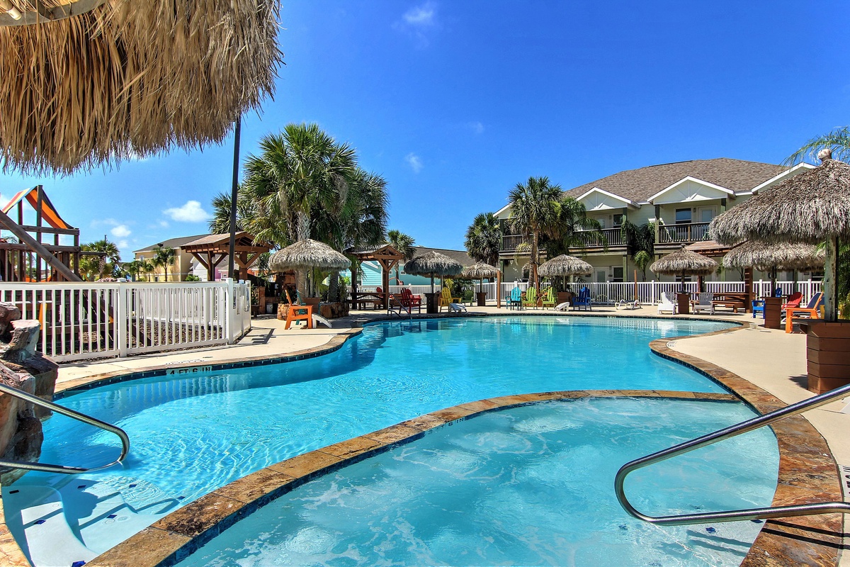 Tropical resort pool area with thatched umbrellas and children's playground under sunny Florida skies.