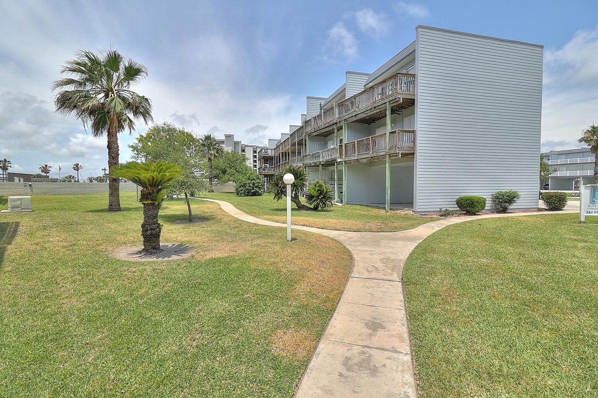 Modern coastal property features multi-level balconies and tropical landscaping with palm trees and manicured lawns throughout the grounds.