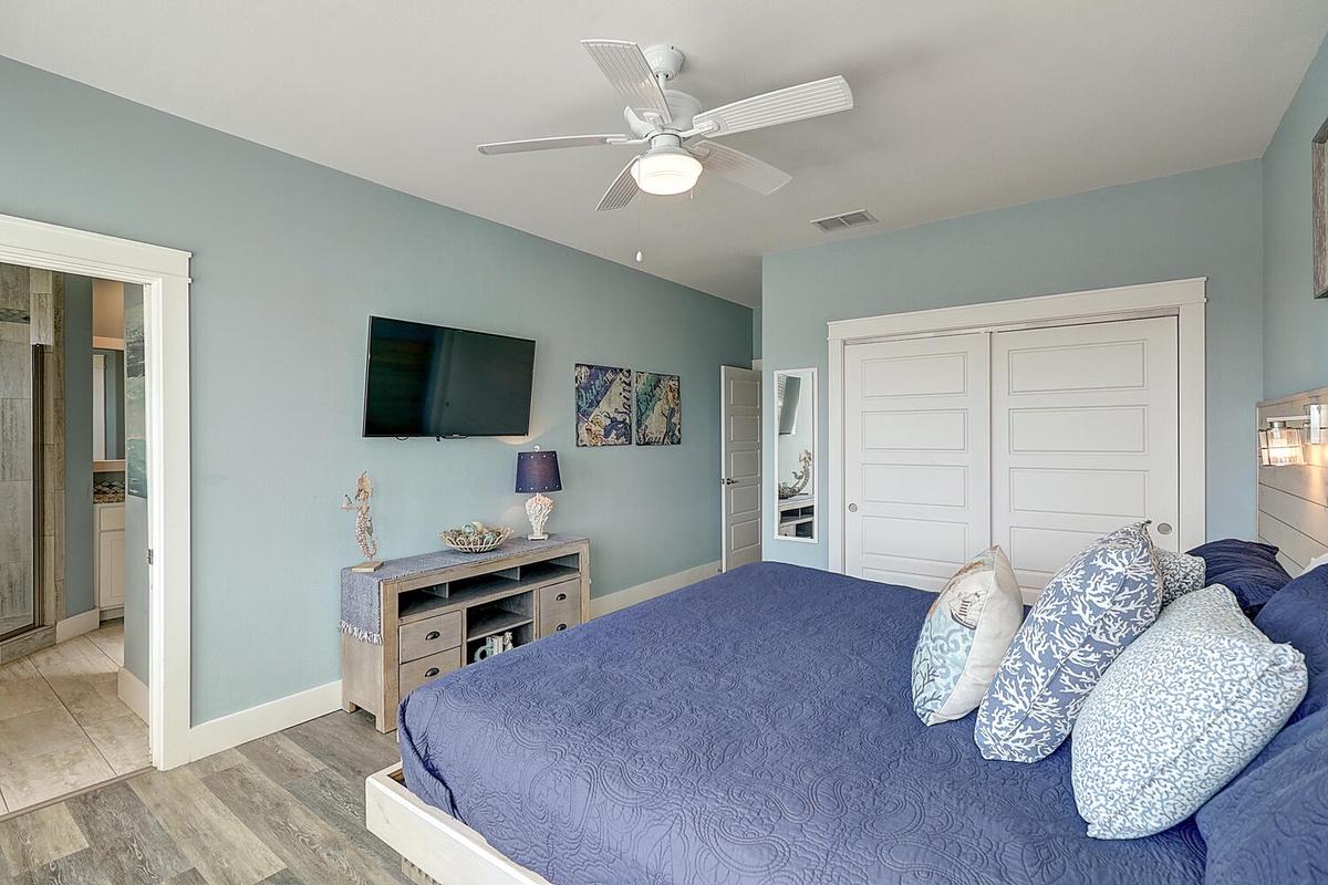 Relax in your serene coastal bedroom with plush bedding, flat-screen TV, and ceiling fan for perfect comfort.
