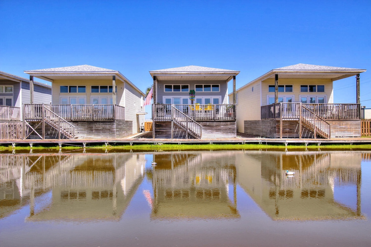 Waterfront vacation rentals with elevated designs reflecting beautifully in calm waters under clear blue skies.