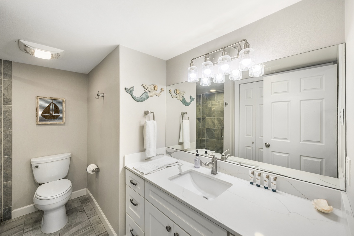 Freshen up in your coastal-themed bathroom with marble counters, bright vanity lighting, and charming mermaid art that sets a whimsical seaside mood.