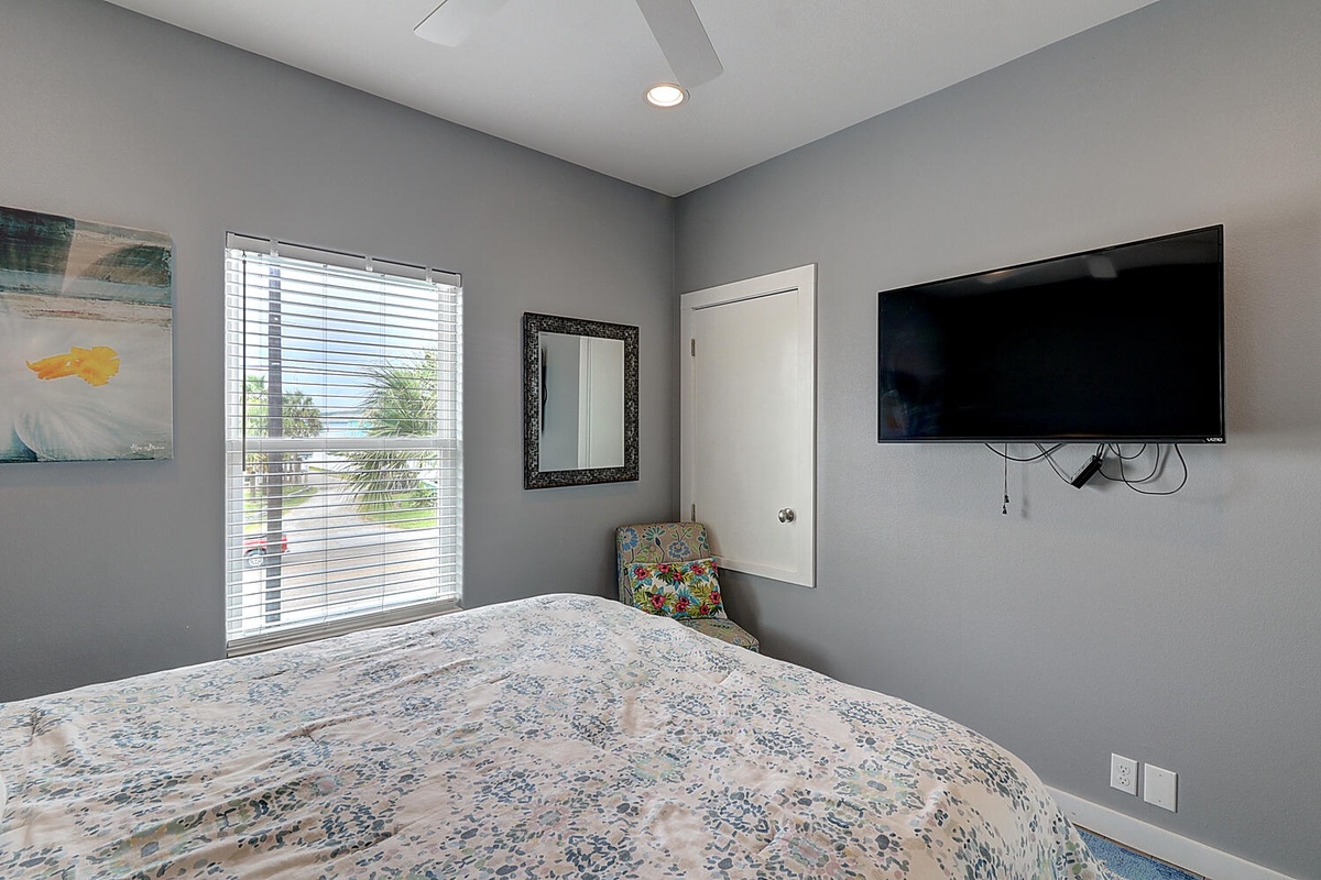 Relax in your peaceful bedroom with cooling ceiling fan, large TV for entertainment, and bright window views of the tropical surroundings.