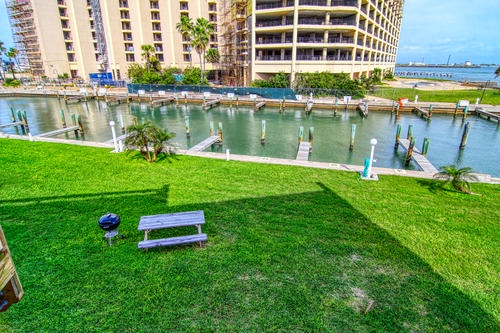 Waterfront property with boat docks, green lawn area, and nearby high-rise buildings along the bay.
