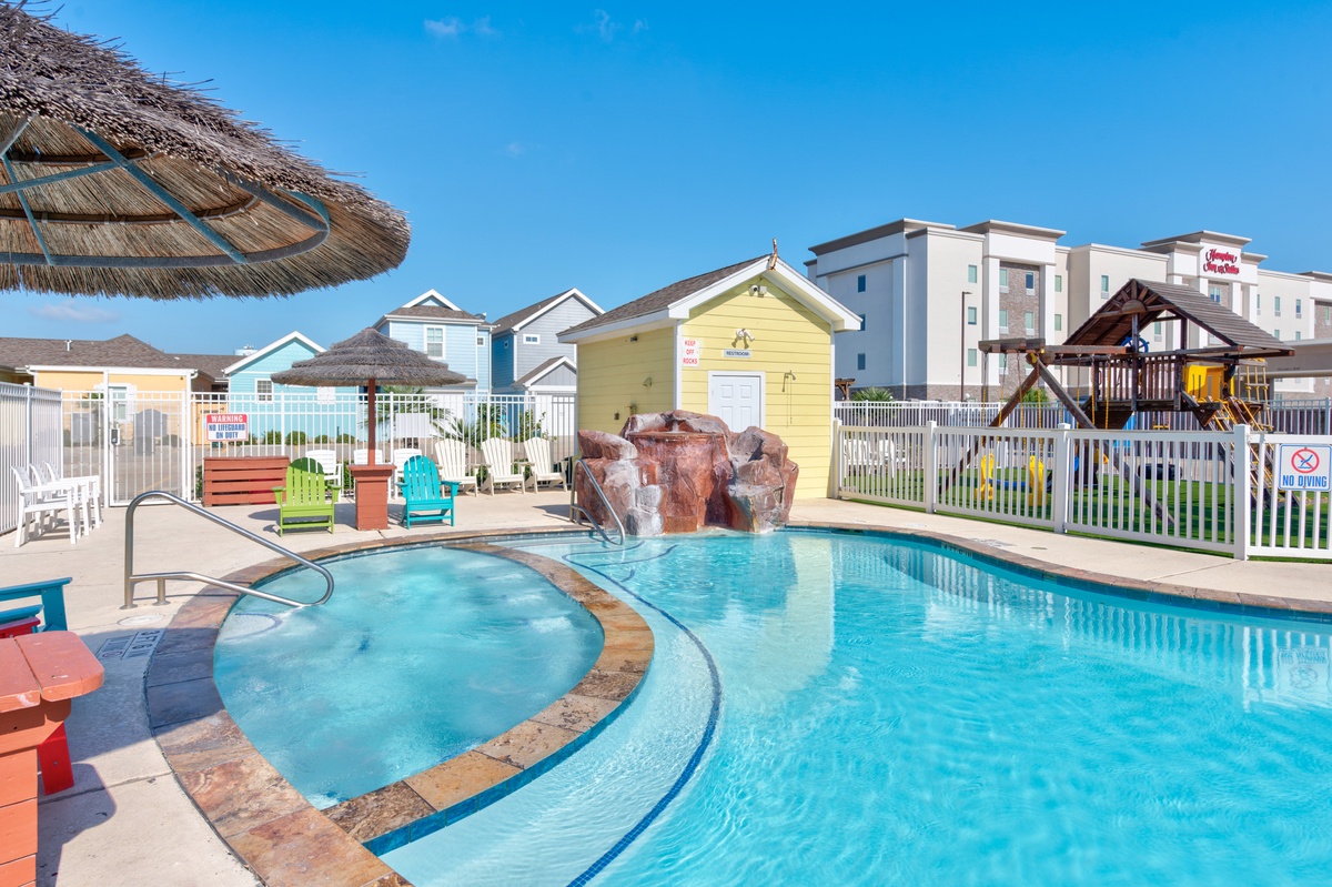 Vibrant pool area with crystal-clear waters, colorful seating, and charming beach cabanas creating a tropical resort atmosphere.