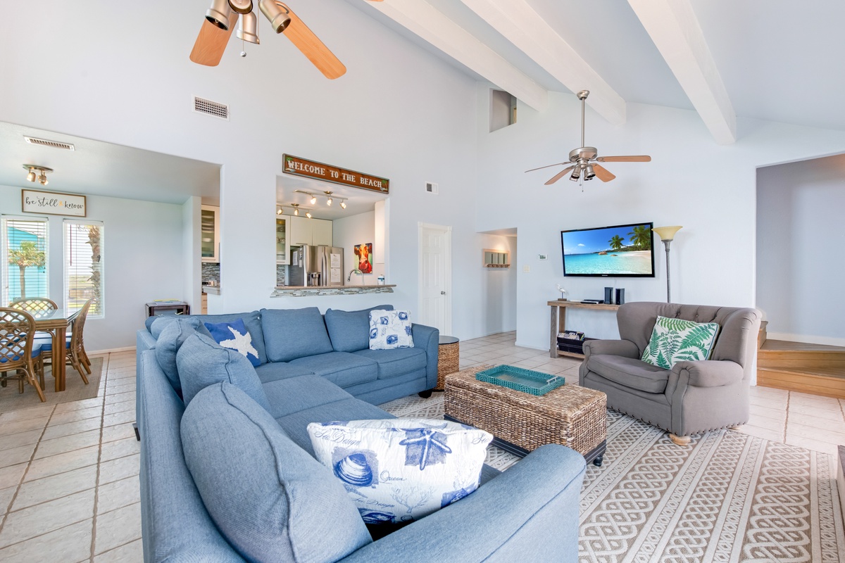 Relax in your bright, coastal-themed living room with vaulted ceilings, blue sectional seating, and entertainment center for memorable evenings.