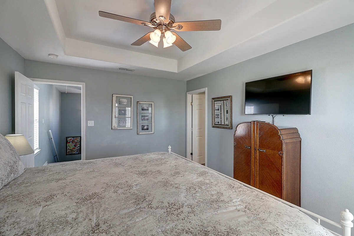 Unwind in your serene bedroom featuring calming blue walls, a vintage dresser, and flat-screen TV for cozy evening entertainment.