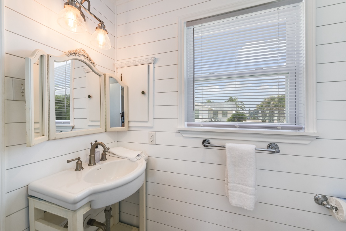 Freshen up in this bright coastal bathroom featuring classic shiplap walls, vintage-inspired fixtures, and a pedestal sink. Soft natural light filters through the window, creating your serene personal retreat.