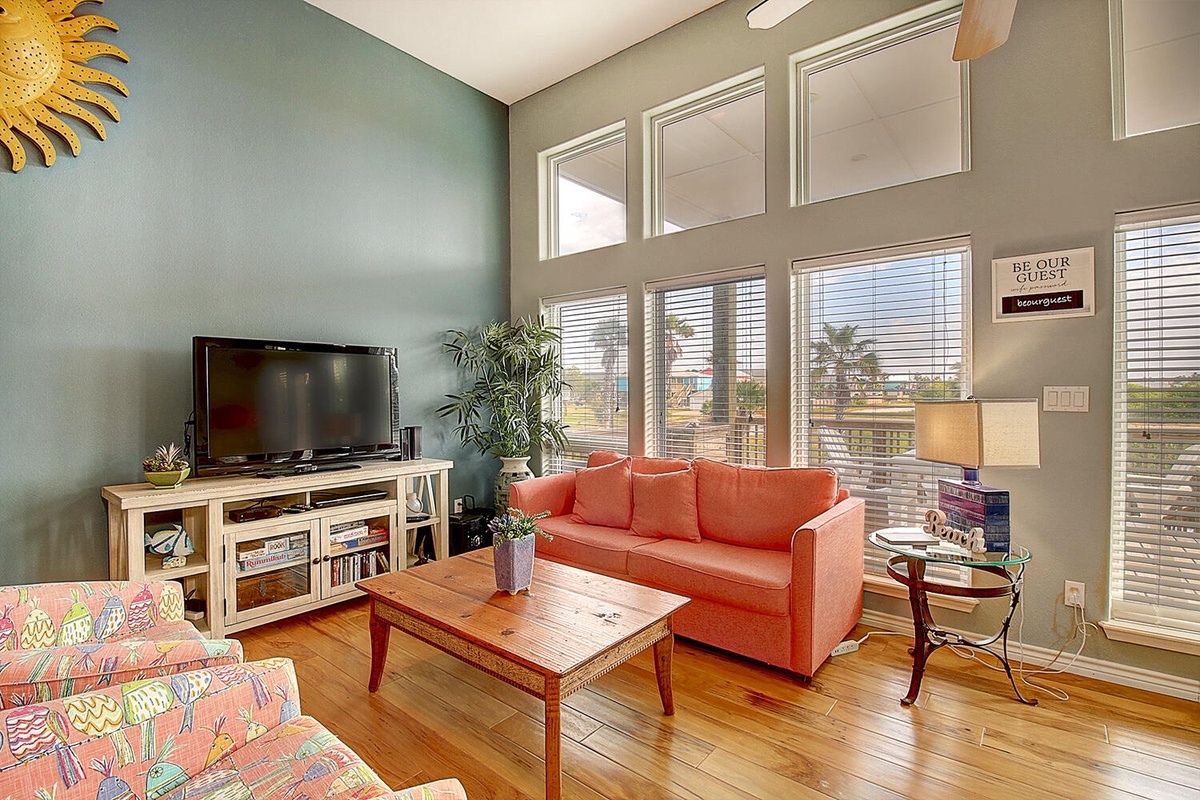 Relax in your bright living room with soaring windows, vibrant coral sleeper sofa, and stunning city views stretching across the horizon.