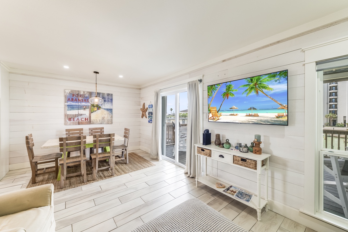 Bright coastal dining area with whitewashed shiplap walls and beach decor. Glass doors flood the space with natural light and open to a private outdoor area ideal for gatherings.