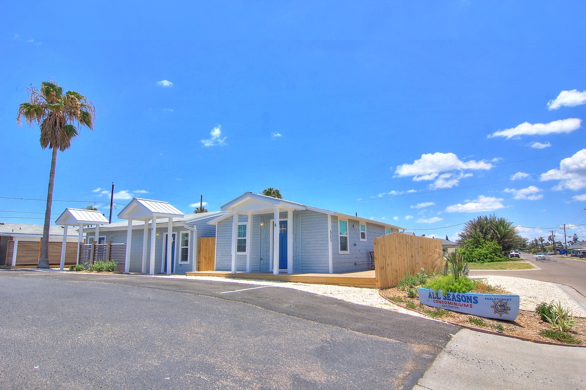 Modern coastal vacation cottages with bright blue trim and tropical palm trees under sunny skies.