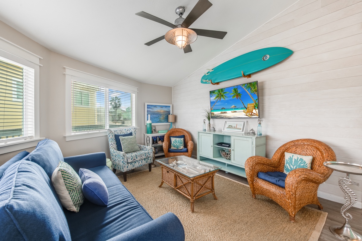 Your coastal living room invites relaxation with nautical charm, featuring comfortable seating and beach-inspired decor under a breezy ceiling fan.