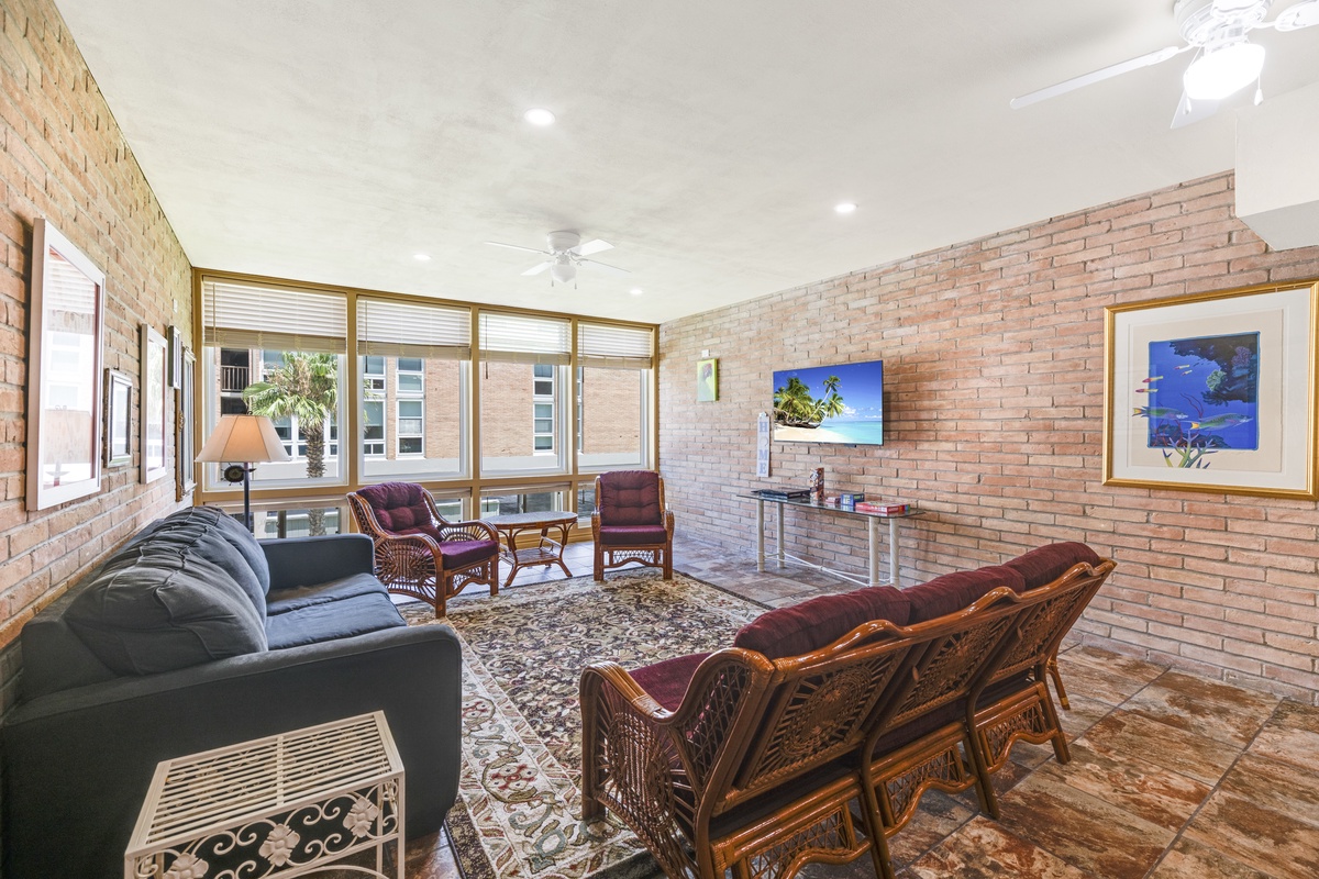 Settle into your private sunroom lounge, where exposed brick walls and ceiling fans create a charming retreat. Relax in comfortable seating while enjoying natural light and garden views through expansive windows.