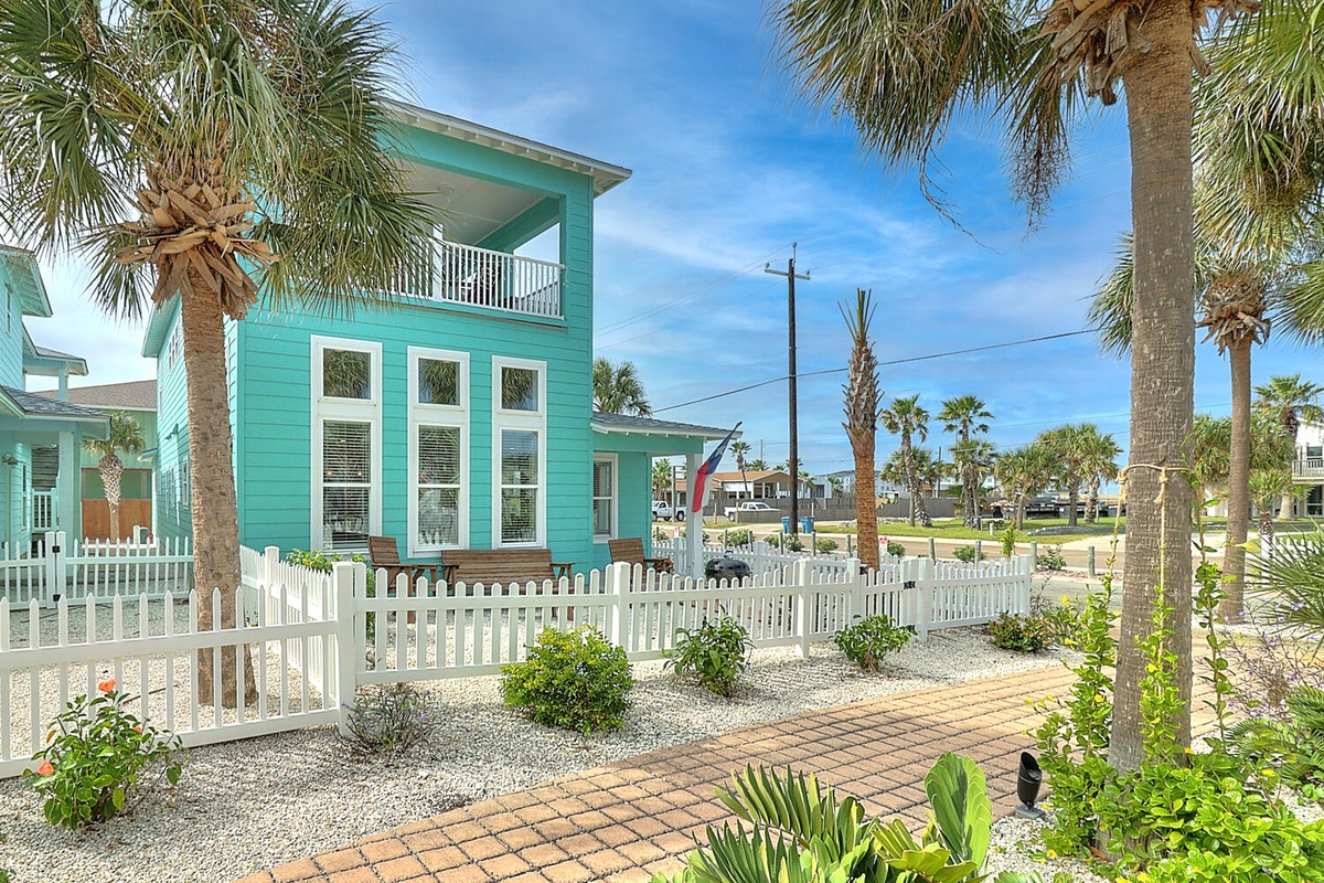 Charming turquoise beach house surrounded by tropical palms and landscaped gardens in a peaceful coastal neighborhood.