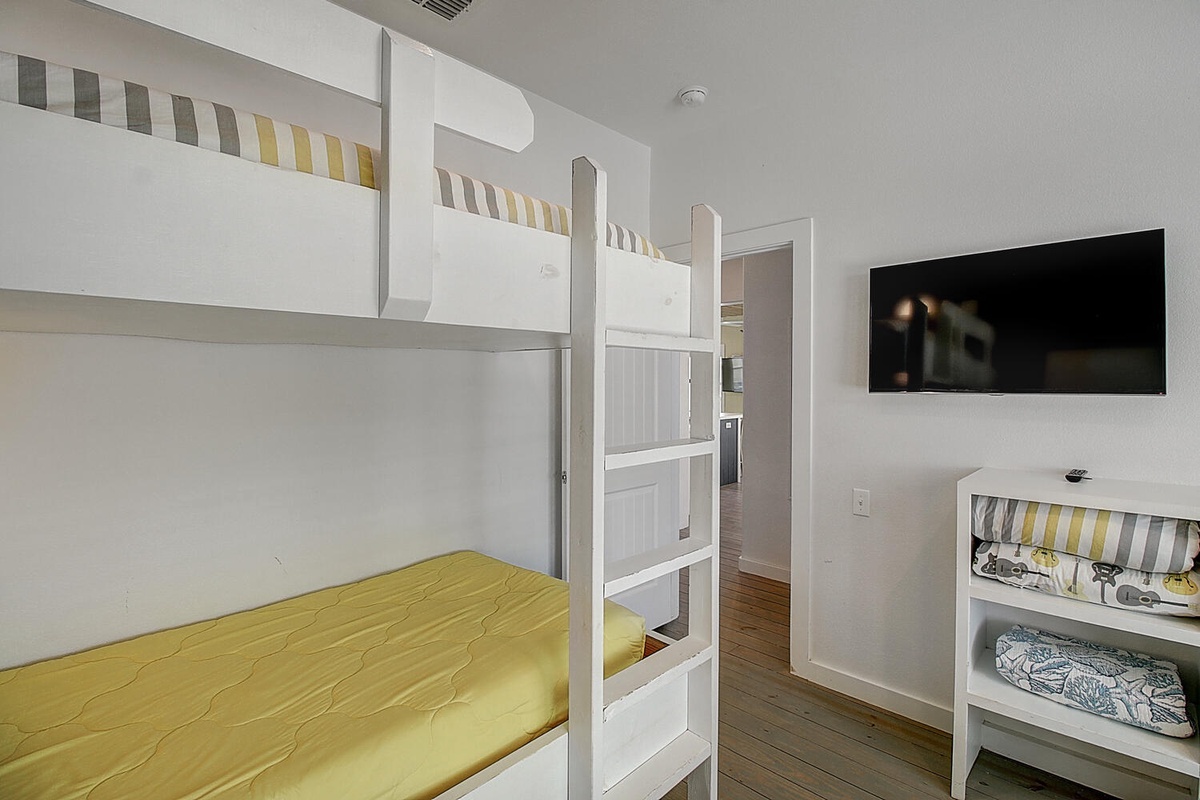 Your family's cozy bunk room features crisp white beds with bright yellow accents and a wall-mounted TV for movie nights together.