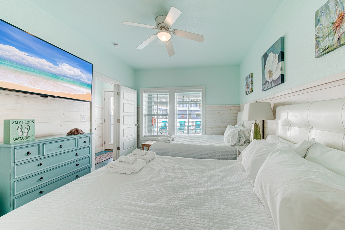 Relax in your coastal-themed bedroom with two comfortable beds, soothing mint accents, and beach artwork creating the perfect seaside retreat.