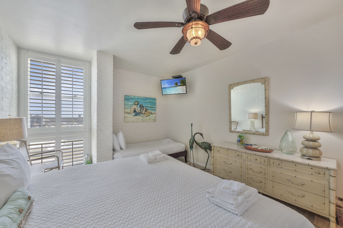 Your serene bedroom features a cozy bed with fresh linens, nautical ceiling fan, and coastal artwork creating the perfect seaside retreat.