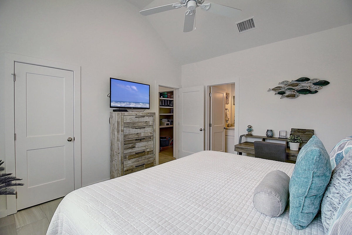Your peaceful bedroom retreat features coastal décor, a wall-mounted TV, and ceiling fan for your comfort during restful nights.