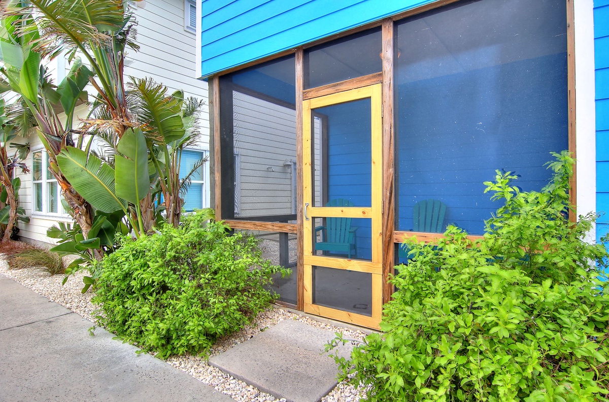 Tropical entrance with lush landscaping and vibrant blue facade welcoming guests to their coastal getaway.