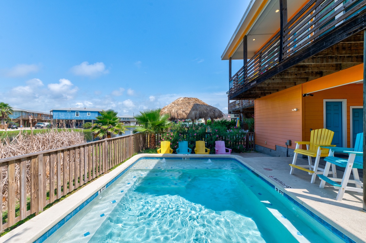 Dive into your private pool surrounded by vibrant Adirondack chairs and tropical palms, with a thatched tiki hut creating perfect shade.