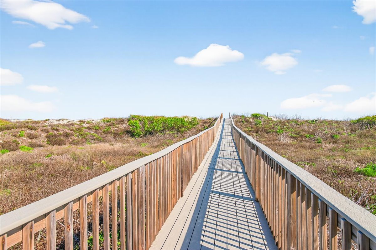 Wooden boardwalk winds through coastal dunes toward the ocean, offering scenic access to natural beach areas.