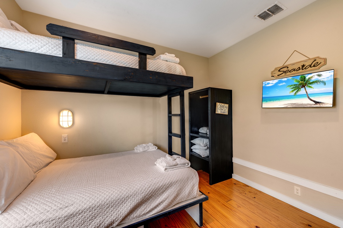 Unwind in your cozy bunk room featuring crisp linens, warm lighting, and tropical beach views on the wall-mounted TV.