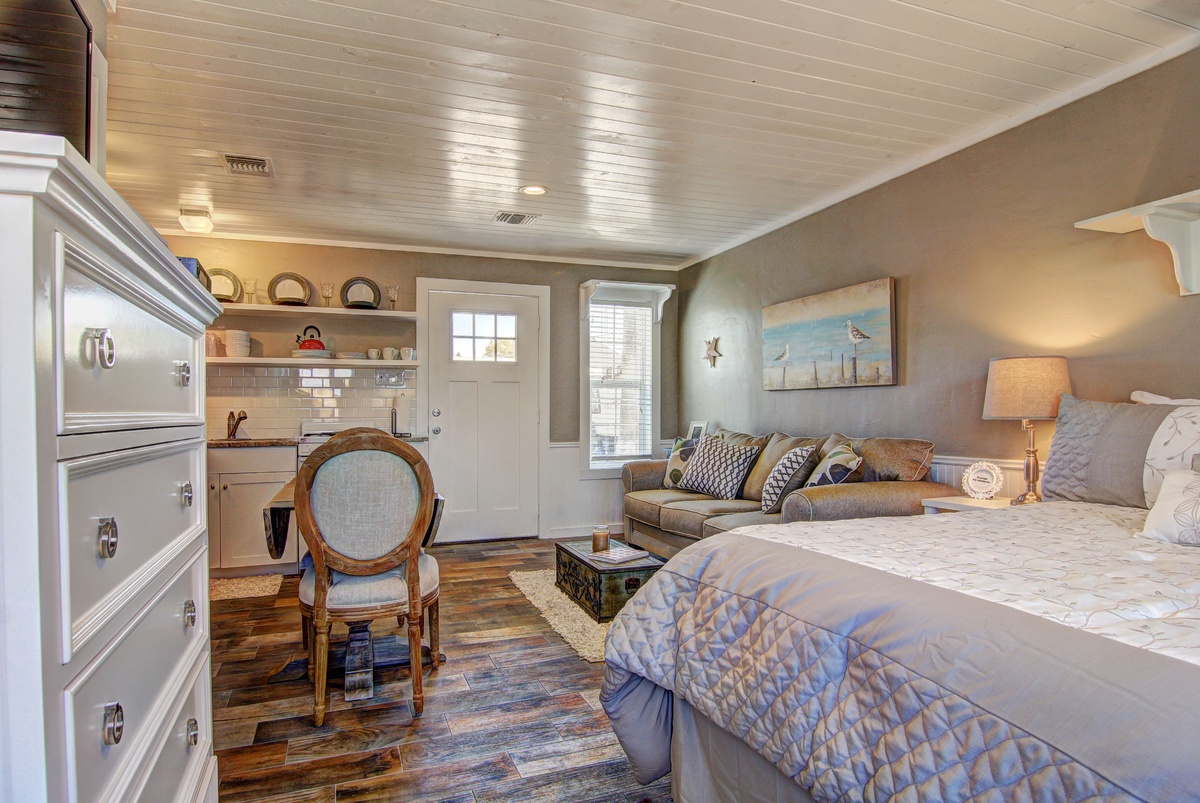 Unwind in your cozy studio where comfort meets coastal charm, featuring a plush bed and inviting living space.
