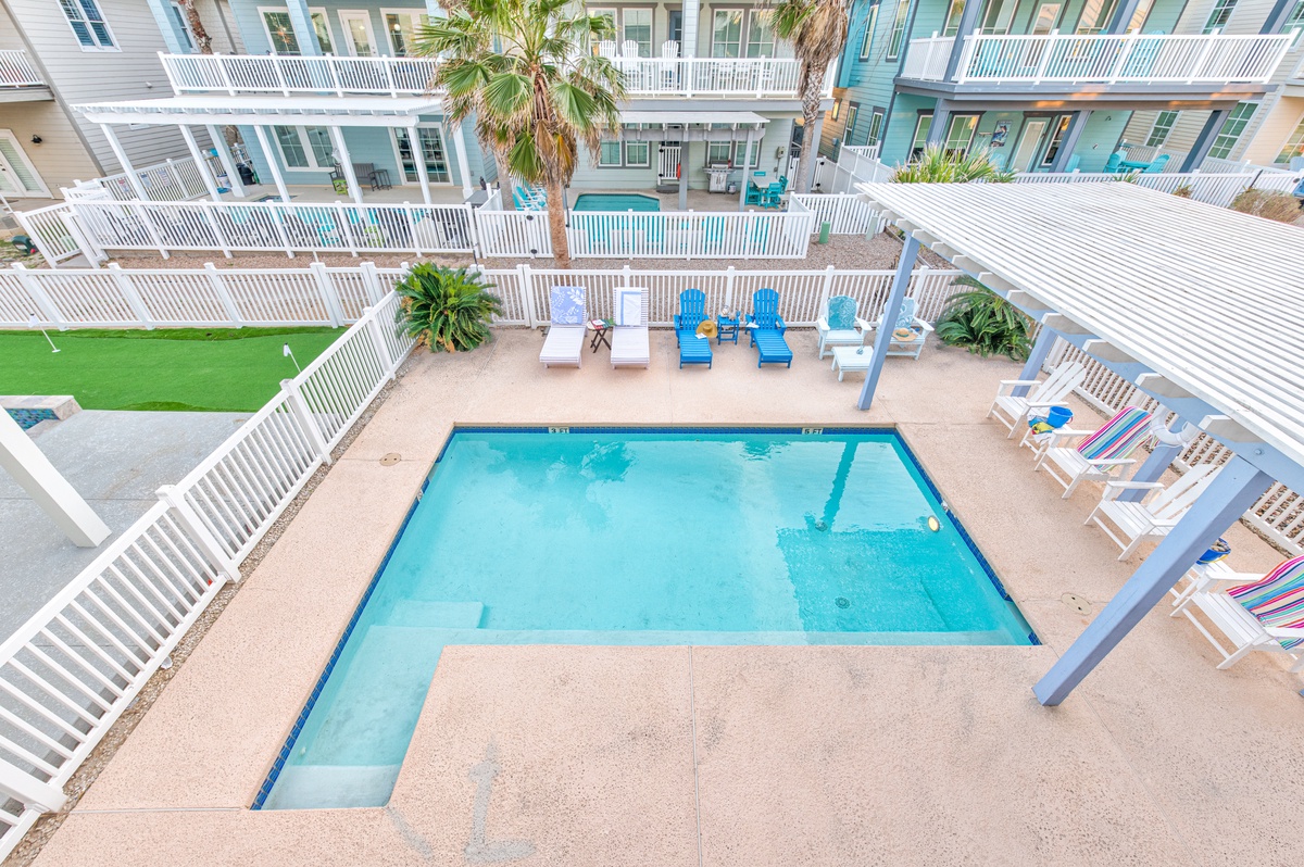 Aerial view of the resort's pool complex surrounded by colorful beach cottages with white railings and tropical palms.