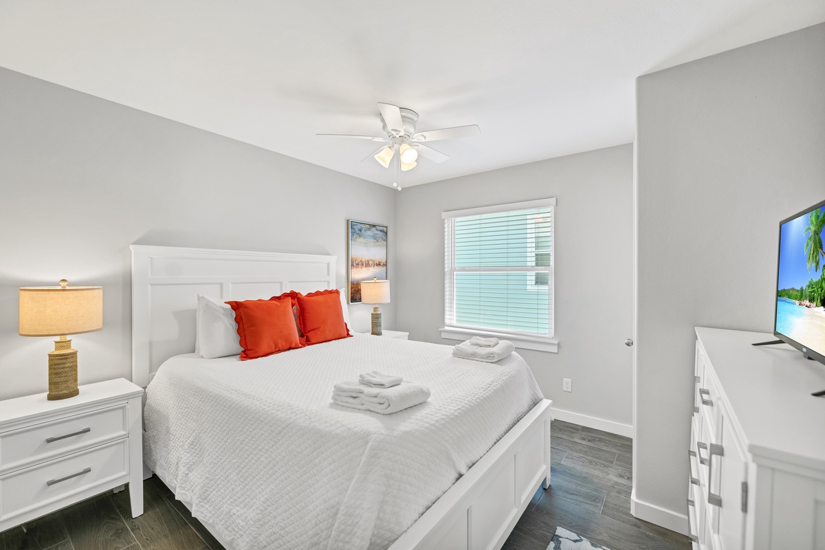 Unwind in your serene bedroom featuring crisp white linens, vibrant accent pillows, and thoughtful touches like fresh towels awaiting your arrival.