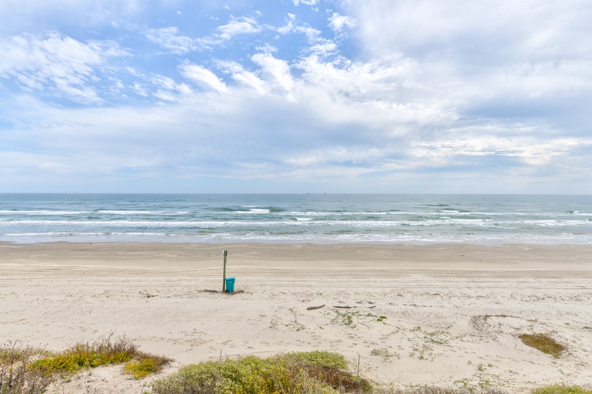 Wide sandy beach stretches along the coastline with gentle waves and dramatic cloudy skies overhead.