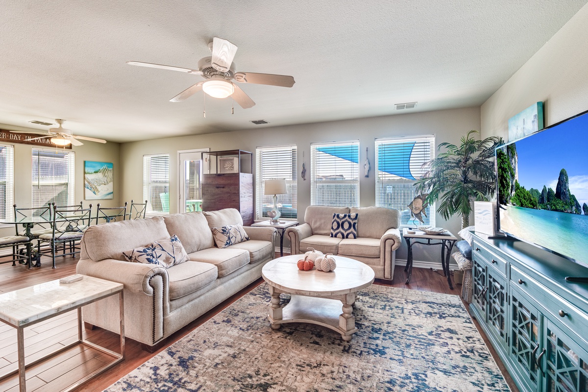 Settle into this spacious living room where coastal elegance meets comfort—plush seating, tropical touches, and a large TV create your perfect retreat.