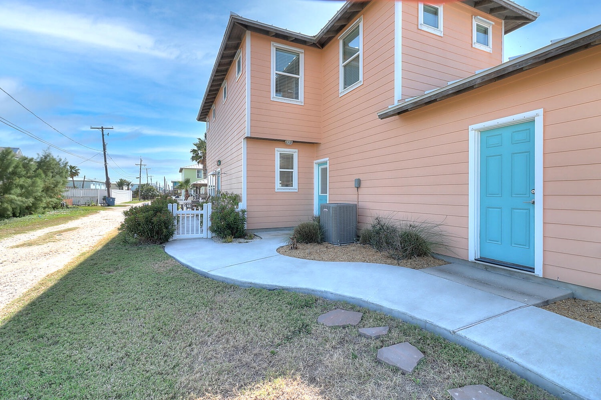 Charming coral-colored property features a welcoming turquoise entrance door and well-maintained landscaping in a peaceful residential setting.