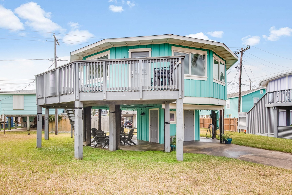 Charming elevated beach house with turquoise siding and wraparound deck in coastal neighborhood.