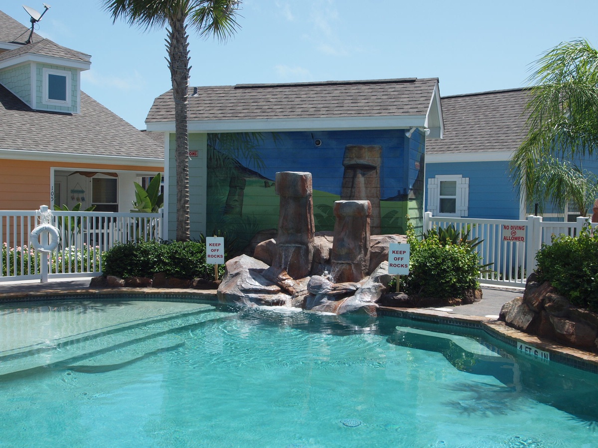 Tropical poolside paradise with crystal-clear waters, decorative rock waterfall, and vibrant coastal-themed buildings surrounding your retreat.