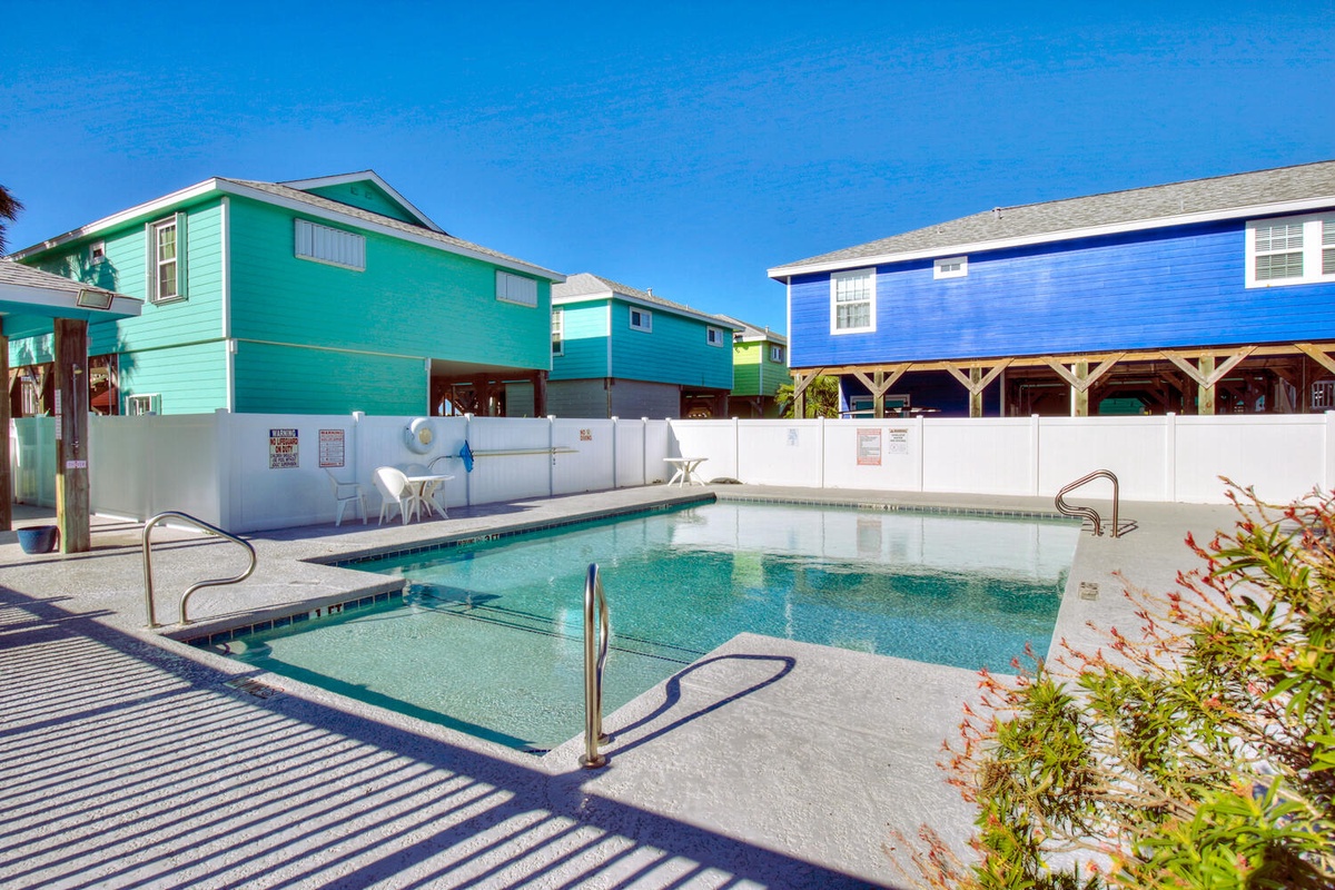 Crystal-clear community pool surrounded by colorful coastal homes under brilliant blue skies.