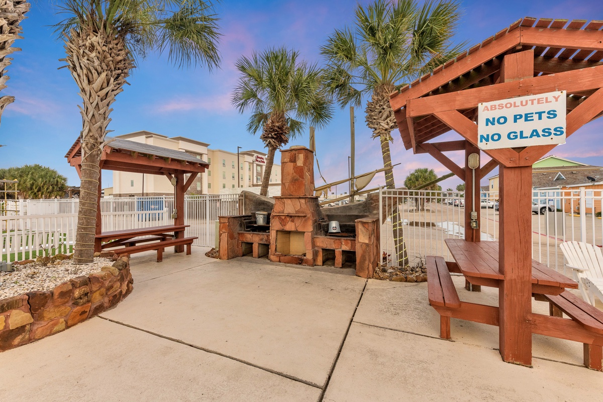 Tropical BBQ pavilion with outdoor fireplace and dining tables surrounded by palm trees at this beachside resort property.