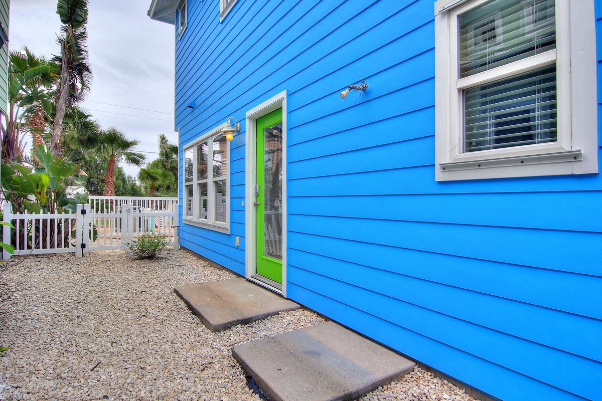 Vibrant blue beach cottage with cheerful lime green door creates a tropical coastal charm in this welcoming neighborhood setting.