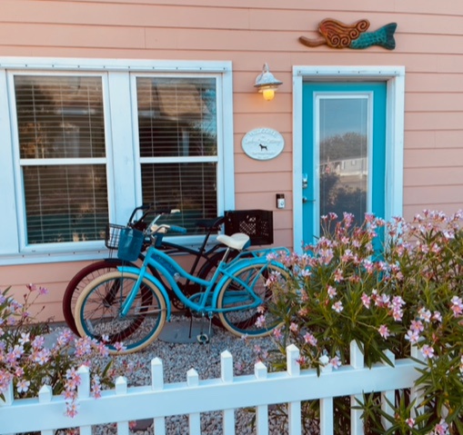 Your charming entrance welcomes you with vibrant turquoise accents and blooming gardens, perfect for coastal getaways.
