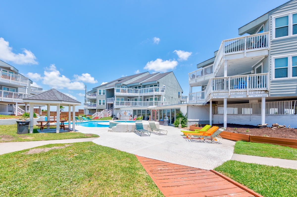 Spacious coastal property featuring multiple buildings, a private swimming pool, and beautifully landscaped grounds under clear blue skies.
