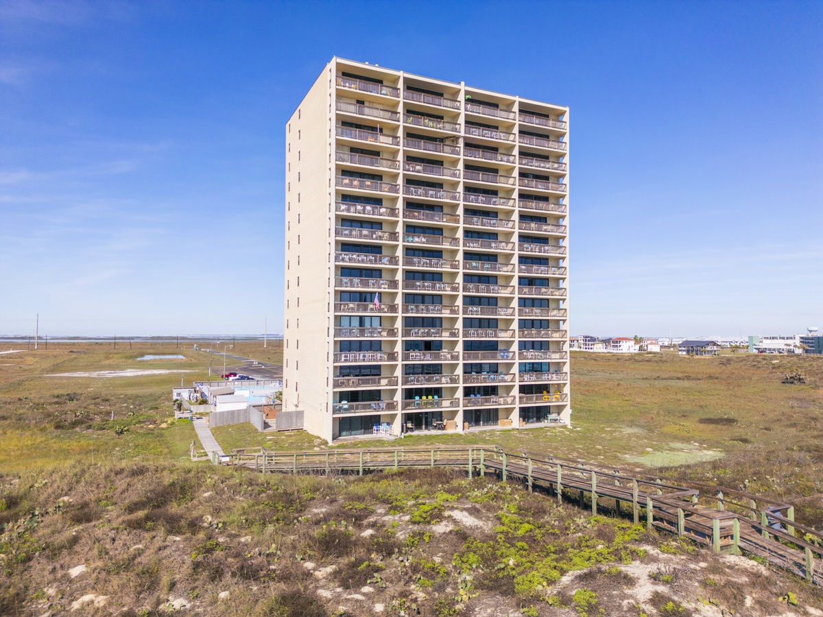 Towering beachfront building surrounded by natural coastal landscape, with wooden boardwalks winding through preserved dune vegetation.