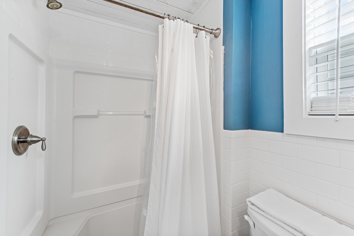 Step into your bright, clean bathroom featuring a spacious tub-shower combo with fresh linens and cheerful blue accents.