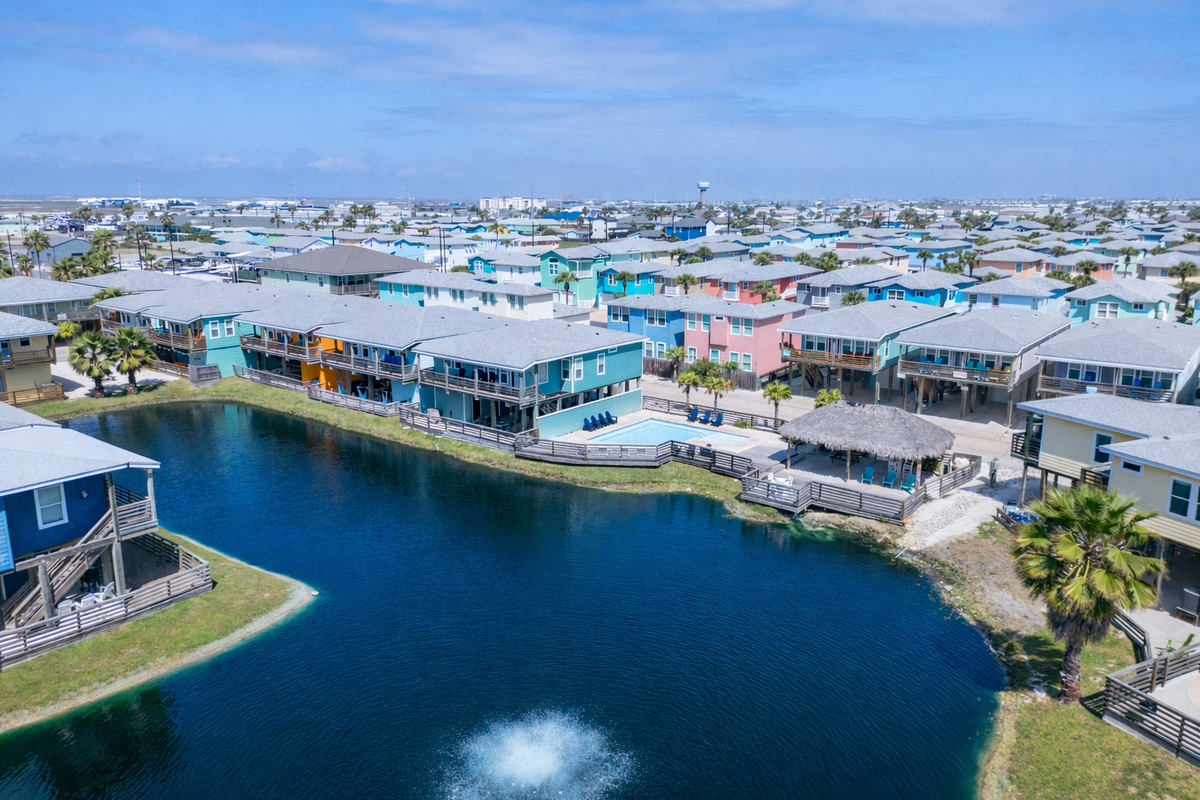 Vibrant coastal community featuring colorful beachfront homes surrounding a peaceful lagoon with tiki hut and waterfront access.