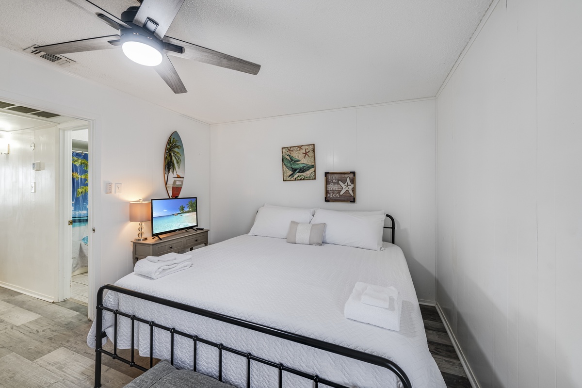 Sink into crisp white linens in your cozy bedroom, complete with tropical artwork and modern amenities for the perfect beach getaway.