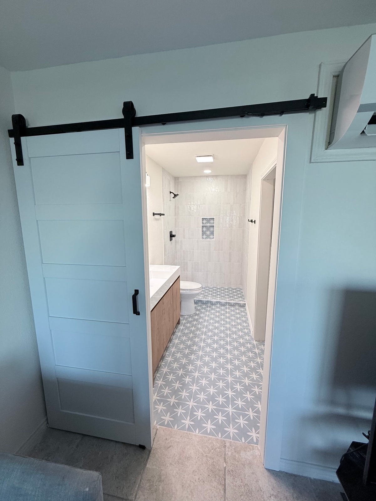 Step into your beautifully designed private bathroom, where a farmhouse barn door reveals sleek modern tile work and a spacious walk-in shower waiting for your morning routine.