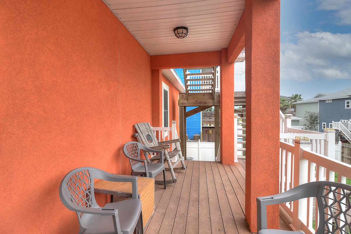 Relax on your private covered balcony with comfortable seating and vibrant coral walls, perfect for morning coffee or sunset drinks.